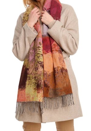 Femme portant un manteau beige tenant une écharpe multicolore à franges avec des motifs abstraits rouges, orange, violets et verts.