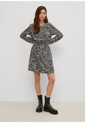 Schwarz-weiß gemustertes Kleid mit langen Ärmeln, tailliertem Bund und weitem Rock, kombiniert mit schwarzen Knöchelstiefeln.
