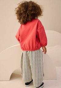 Červená mikina s elastickým lemem, spárovaná s kalhotami s širokými nohavicemi v černobílých pruzích. Černé tenisky doplňují outfit.