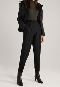 Doudoune noire, col roulé côtelé olive, pantalon noir taille haute sur mesure, et bottines noires à bout pointu avec une finition lisse.