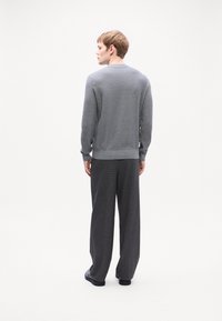 Pulover gri texturat cu guler rotund, combinat cu pantaloni lejeri de un gri închis. Design simplu, minimalist, fără modele suplimentare.