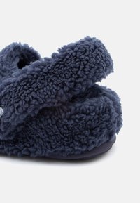 Σκούρο μπλε αέρινη παντόφλα με πλούσια υφή στο επάνω μέρος και φαρδύ λουρί κατά μήκος της κορυφής, σχεδιασμένη για άνεση μέσα στο σπίτι.