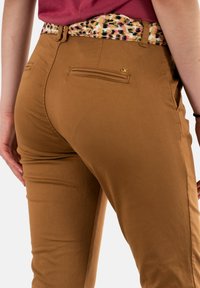 Pantaloni casual marroni con un design aderente, caratterizzati da una vita decorata e due tasche posteriori. Tessuto morbido, versatile per diversi outfit.