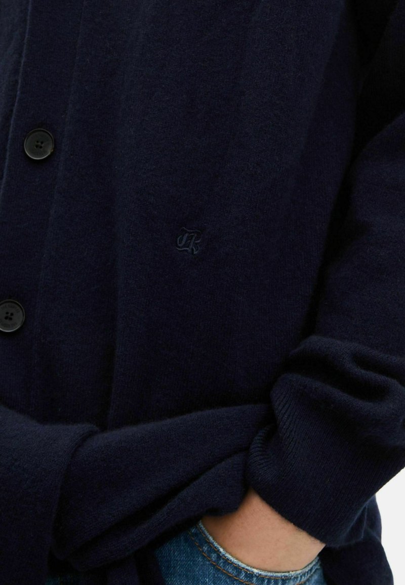 Navy cardigan made of soft fabric, featuring a button-up design, ribbed cuffs, and an embroidered logo detail on the left chest.