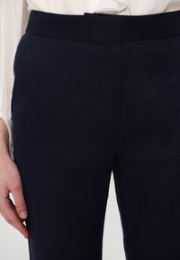 Navy blue tailored trousers with a smooth texture and flat waistband. Features side pockets and a streamlined design for a fitted look.