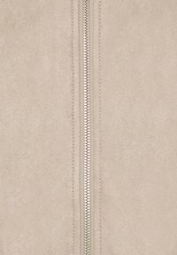 Chaqueta de ante beige con una cremallera central plateada, textura suave y un diseño limpio y minimalista sin patrones ni acentos adicionales.