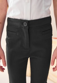 Musta housut, joissa on nappisuljenta, etukulmataskut ja sileä kangaspinta. Suunniteltu mukavuutta ja istuvaa leikkausta varten.