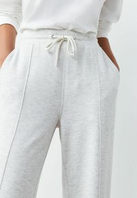 Hellgraue Jogginghosen aus weichem, strukturiertem Stoff. Mit Kordelzugbund, Seitentaschen und kontrastierenden Paspeln an den Nähten.