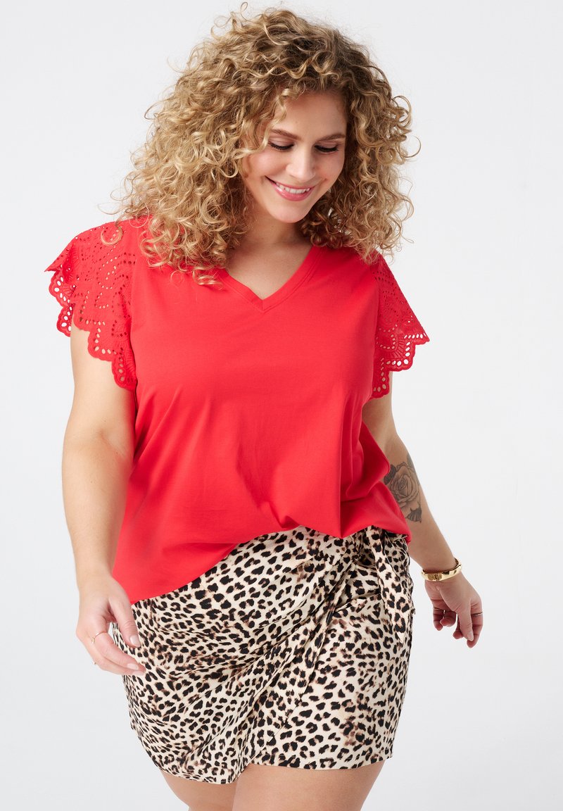 Rotes V-Ausschnitt-Oberteil mit Wellenkante aus Spitze, kombiniert mit einem Leopardenmuster-Rock. Das Outfit zeichnet sich durch eine lockere Passform und glatte Texturen aus.