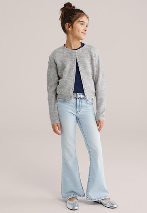 Cardigan gris en maille avec encolure ronde, fermeture par boutons, associé à un jean évasé bleu clair et des ballerines argentées. Design simple et texturé.