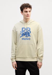 Felpa beige con cappuccio e tasca a marsupio, stampa grafica blu con un toro e il testo "HUGO", polsini e orlo a coste.