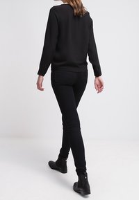 Svart långärmad topp i slät tyg, kombinerad med åtsittande svarta jeans och ankelboots, som visar upp en minimalistisk, sömlös design.