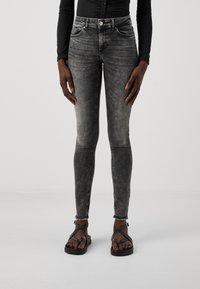 Jeans skinny negros desgastados con una textura suave, diseño de cinco bolsillos y dobladillos deshilachados, combinados con sandalias negras de tiras.
