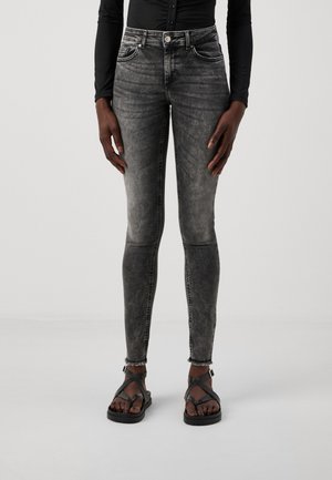 Faded black skinny jeans with a smooth texture, five-pocket design, and frayed hems, paired with black strappy sandals.