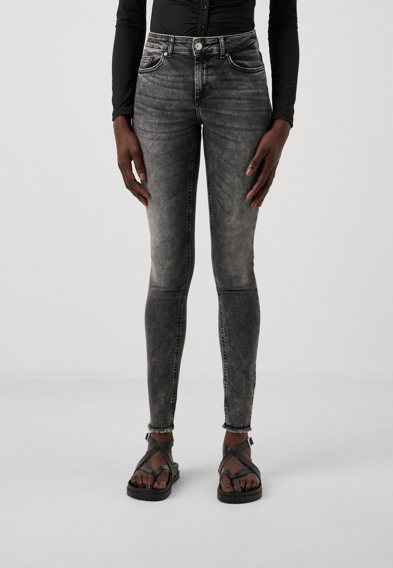 Jeans skinny negros desgastados con una textura suave, diseño de cinco bolsillos y dobladillos deshilachados, combinados con sandalias negras de tiras.