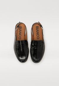 Svart lærs slip-on sko med glatt finish, med loafers design, og en sølvfarget spenne på hælen. Brun såle med logo.