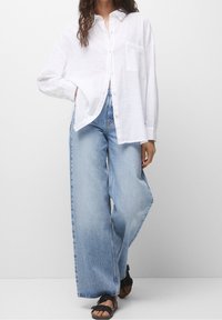 White linen button-up shirt with a chest pocket, paired with light blue high-waisted wide-leg jeans and black sandals.