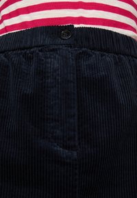Falda de pana azul marino con acanalado vertical, con una cinturilla elástica y un detalle de botón negro. Parte superior a rayas visible por encima de la falda.