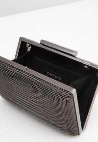 Elegantní psaníčko z kovové síťoviny v černé a stříbrné barvě s pevnou konstrukcí, zapínáním na sponu a černou látkovou podšívkou s vnitřní značkou.