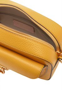 Žlutá texturovaná kožená crossbody taška se zlatými kovovými prvky a zipovým uzavřením. Interiér obsahuje tlumenou podšívku a značkovou etiketu.
