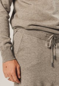 Strickpullover und Jogginganzugset in hellbeige, mit gerippten Bündchen, Kordelzugbund und glatter Textur. Nahaufnahme der Stoffdetails.