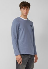 Lange mouwen shirt in lichtblauw katoen, met een ronde halslijn en een klein zwart logo op de linkerborst. Gladde structuur en aansluitend ontwerp.