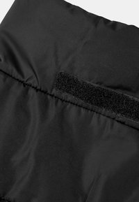 Zwarte, gestructureerde stof met zichtbare stiksels en een klittenbandstrip. Het materiaal lijkt duurzaam en waterafstotend.