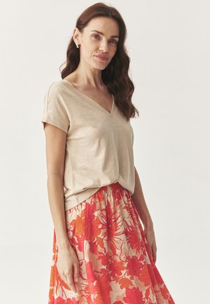 T-shirt beige leggero con scollo a V abbinato a una gonna fluida a fantasia floreale nei toni dell'arancione, con vita elastica.