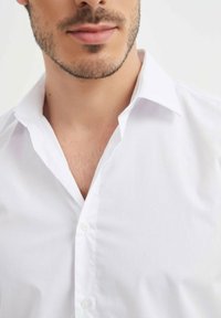 Chemise blanche à col, en tissu lisse et texturé, dotée d'une patte de boutonnage et d'un design classique. Col légèrement replié.