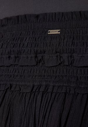 Falda negra con una cintura fruncida que presenta volantes y una etiqueta metálica de la marca. La tela parece ligera y texturizada.