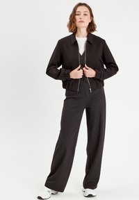 Veste bomber noire courte avec un col, des poignets élastiques et une fermeture éclair devant, assortie à un pantalon large à rayures noires et blanches. Baskets blanches.