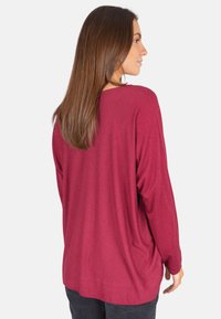 T-shirt bordeaux à manches longues avec une coupe ample, un col rond et une texture lisse. L'arrière présente un design àOurlet incurvé.