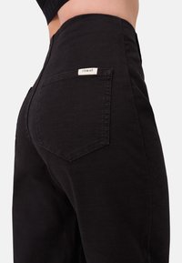 Zwarte denim broek met hoge taille, een achterzak met label en een getextureerde stof voor duurzaamheid. Eenvoudig en klassiek ontwerp.
