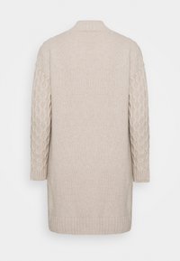 Largo vestido de suéter de punto beige con patrón de trenzas en las mangas, puños acanalados, dobladillo y cuello tipo alto, mostrado desde atrás.