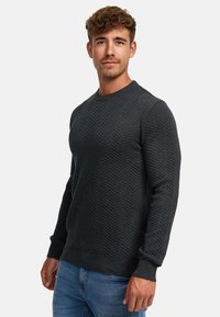 Mørkegrå striktrøje med et fiskebensmønster, rund hals og ribbede manchetter og kant. Båret over blå jeans.