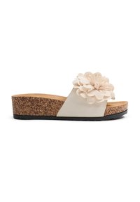 Sandalias tipo slide con suela de corcho, que presentan un upper de tela crema con un acento de flor de gran tamaño, diseño plano y suela de goma texturizada.