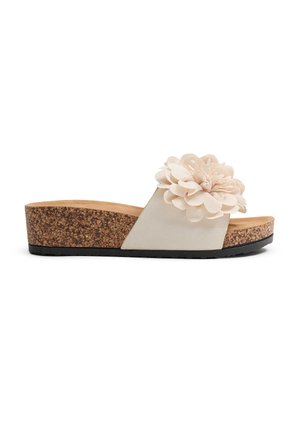 Sandalias tipo slide con suela de corcho, que presentan un upper de tela crema con un acento de flor de gran tamaño, diseño plano y suela de goma texturizada.
