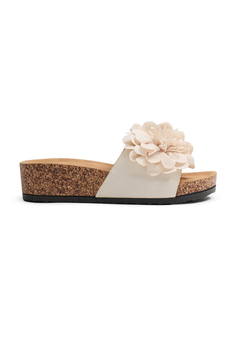 Sandalias tipo slide con suela de corcho, que presentan un upper de tela crema con un acento de flor de gran tamaño, diseño plano y suela de goma texturizada.