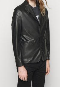 Svart läderblazer med en strukturerad design, enkel ventil, notch lapeller, två framfickor och en slät, något glansig yta.