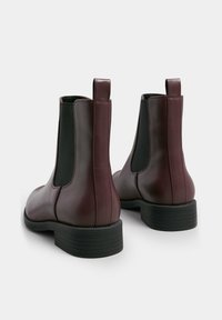 Bottes en cuir bordeaux jusqu'aux chevilles avec des panneaux élastiques latéraux noirs, une languette de tirage et une semelle en caoutchouc noir texturée. Fini lisse et bout rond.
