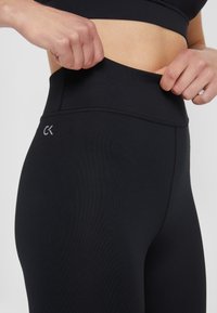 Černé legíny s vysokým pasem vyrobené z elastického materiálu, se seaming designem a malým logem na pásku.