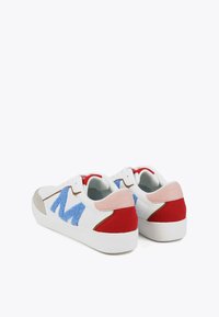 White sneakers with multicolored accents: blue fluffy 'M', red and pink suede, grey suede toe cap, and white rubber sole.