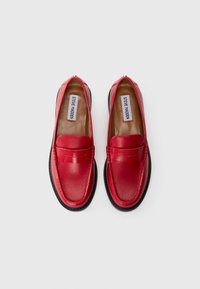 Red leather loafers with a rounded toe and stitched detailing. Features a flat black rubber sole and a smooth, shiny finish.