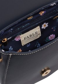 Innenseite einer marineblauen Ledertasche mit blühendem Futter, goldenem Reißverschluss und einem Stoffetikett mit der Aufschrift "FABLE ENGLAND."