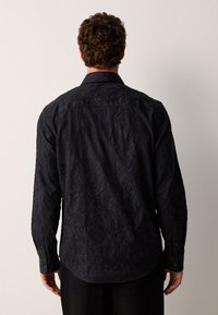 Schwarzes Langarmhemd mit strukturierten Blattmustern, geknöpften Manschetten und abgerundetem Saum, aus leichtem Stoff gefertigt.