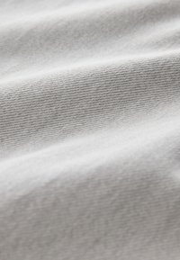 Gros plan d’un tissu doux gris clair avec un tissage fin et de subtils plis montrant la texture et un tombé délicat.