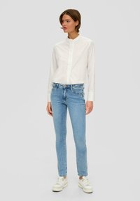 Witte langemouwenshirt met een Mandarin-kraag, gecombineerd met lichtblauwe slim-fit jeans en witte sneakers. Eenvoudig ontwerp, geen zichtbare patronen.