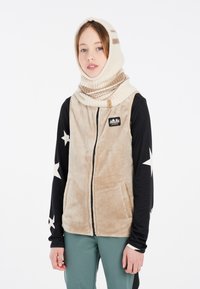 Beige Fleece-Weste mit schwarzen langen Ärmeln, die mit weißen Sternmustern verziert ist. Das Modell trägt eine cremefarbene gestrickte Kapuze mit braunen Streifen.