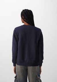 Sudadera azul marino con cuello redondo, mangas largas y puños y dobladillo de canalé. Textura suave, diseño sencillo, sin patrones visibles.