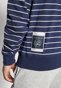 Navy and white striped cotton sweatshirt with a ribbed hem and cuffs. Features a fabric label with New York Yankees branding.